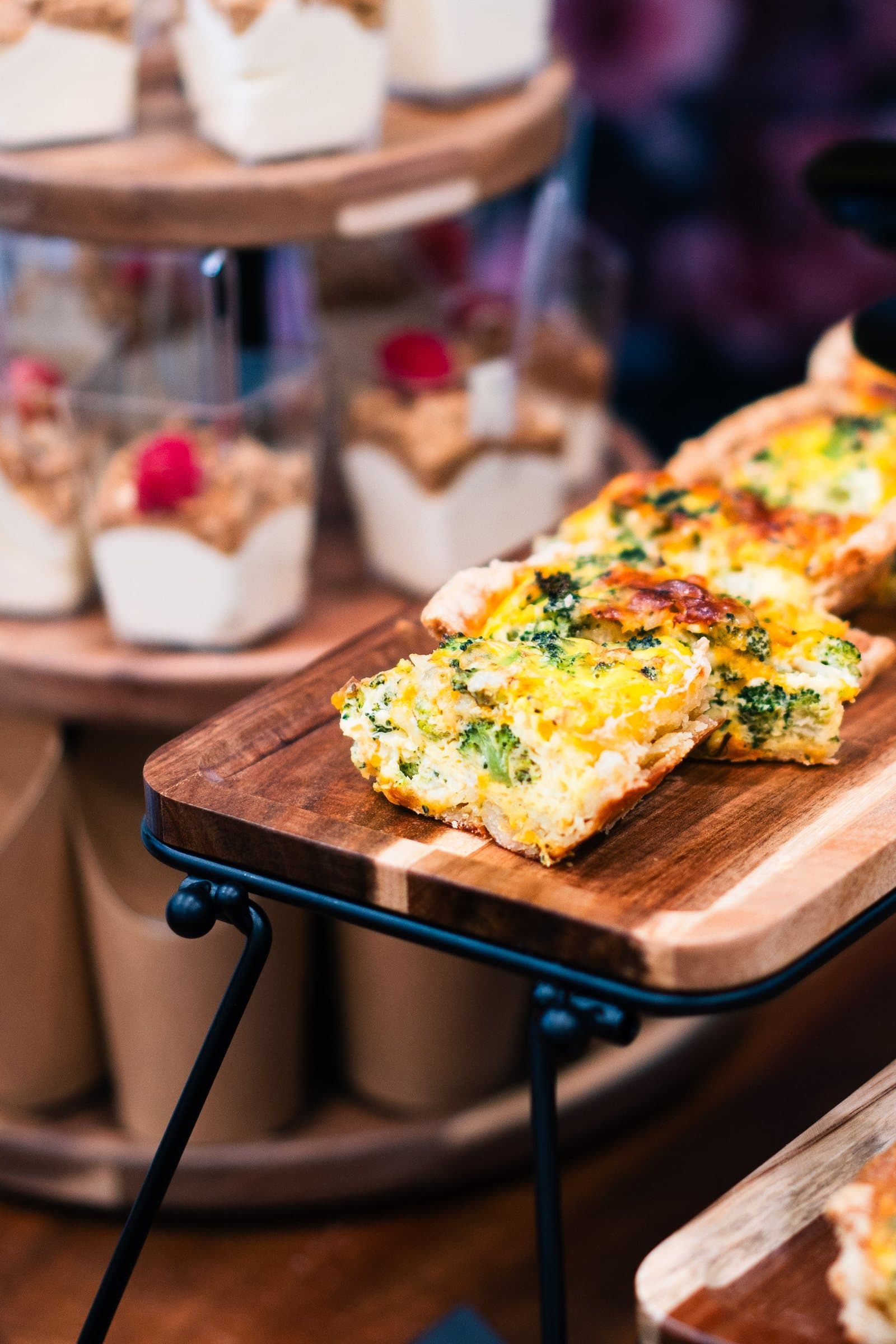 Quiche slices on a wooden riser with desserts behind, styled food photography