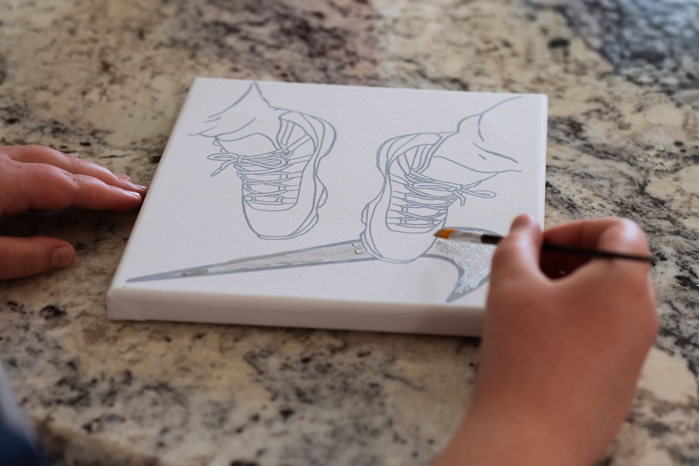 Artist painting a pre-drawn sneaker canvas from a DIY paint kit