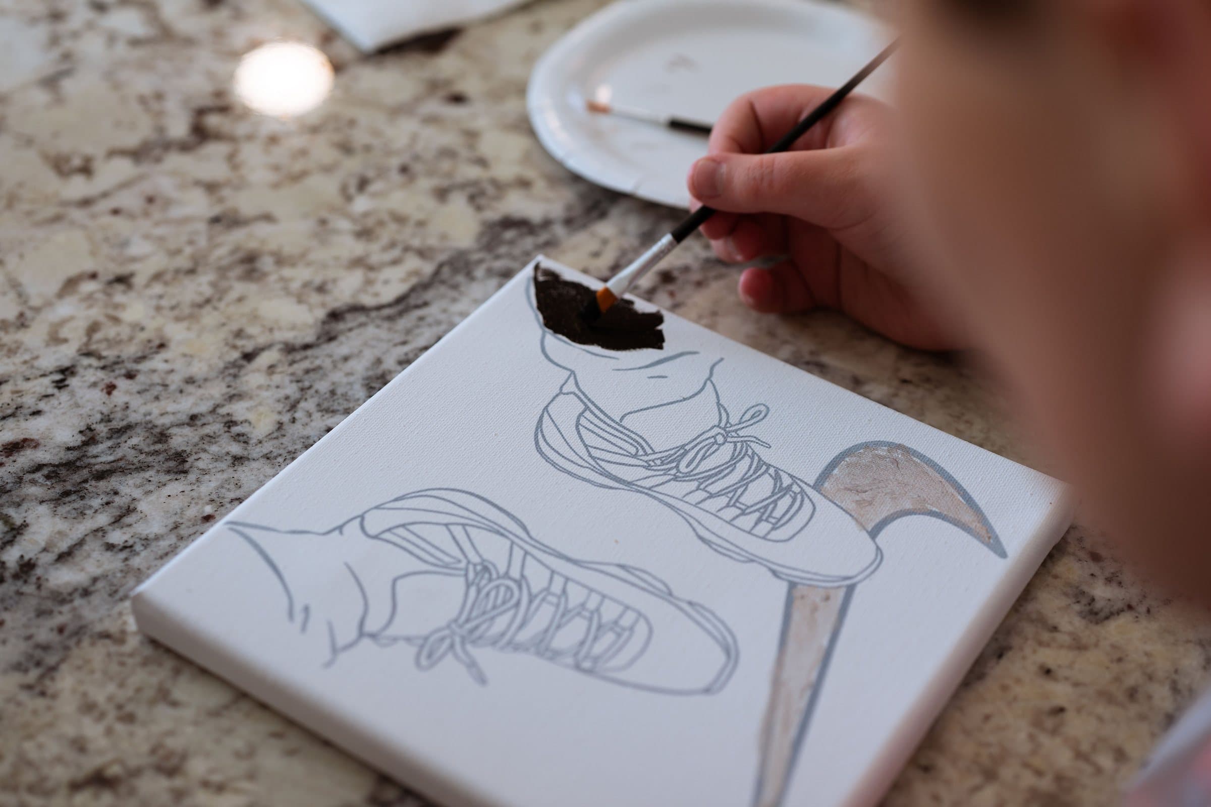 Close-up of a brush adding color to a canvas sneaker design