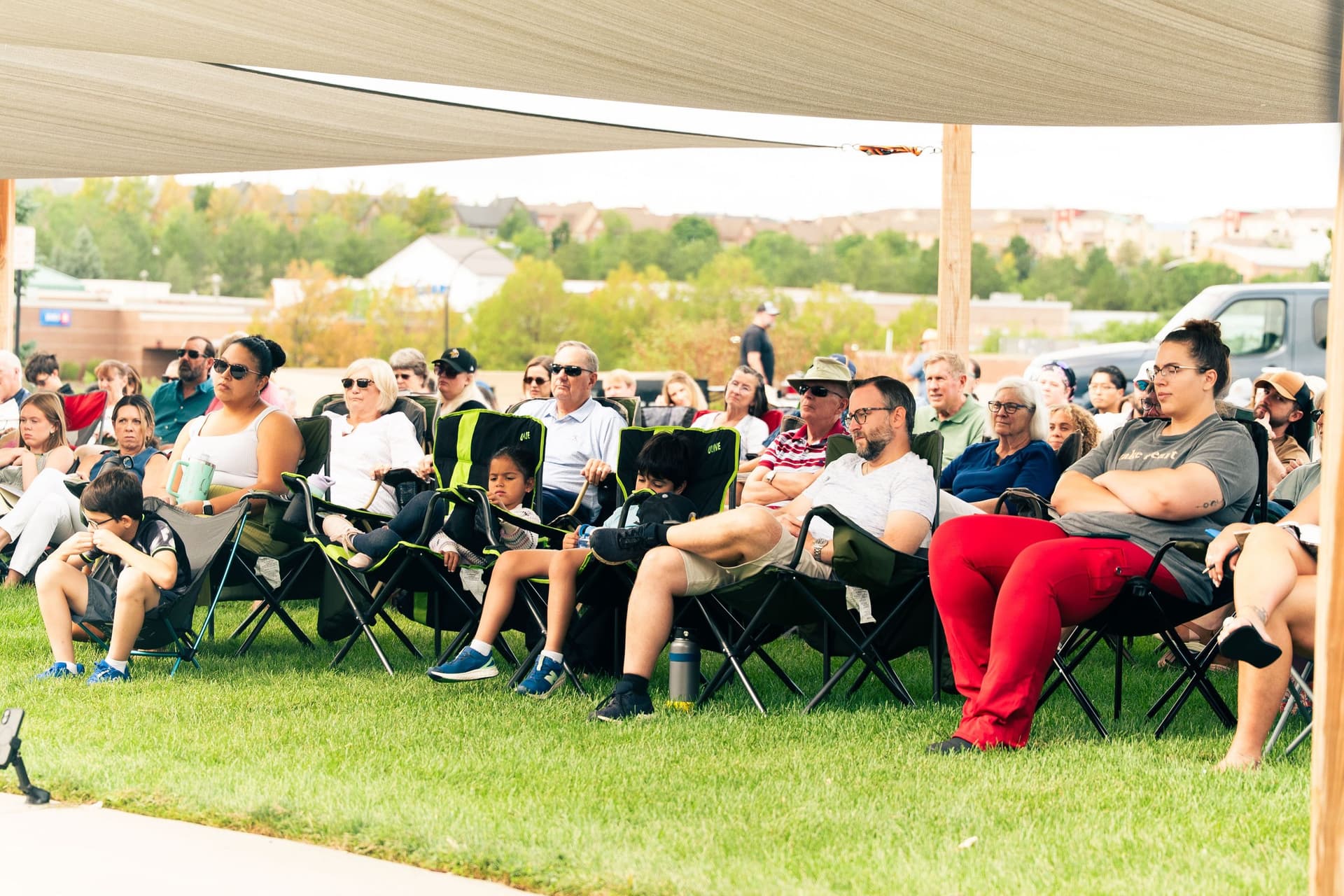 Guests seated under shade sails listening at an outdoor church service