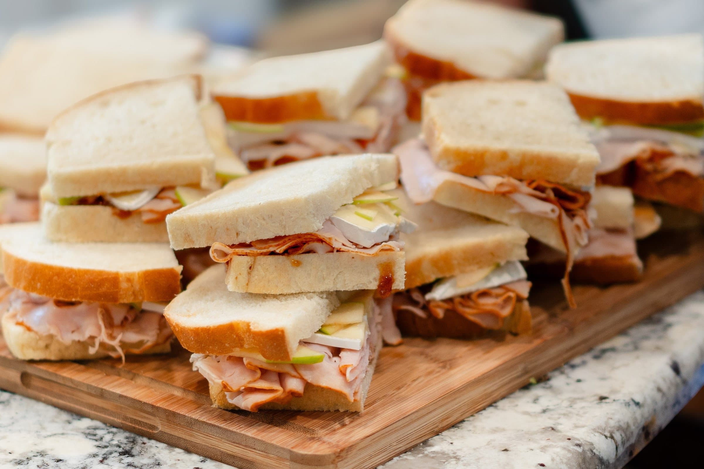 Finger sandwiches arranged on a wooden serving board, catering food photography